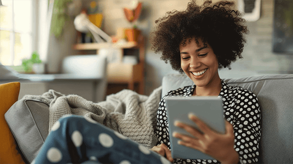 Smiling woman wearing a polka dot blouse enjoying an E-reader on cozy sofa at home